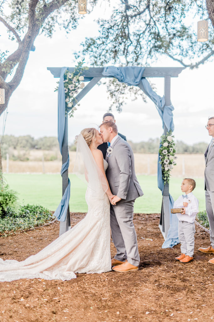 Wedding Ceremony First Kiss Dusty Blue Arch | Stonehouse Villa in Driftwood TX by DFW Dallas Fort Worth wedding photographer Karina Danielle Photography