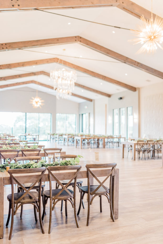 Reception Hall Chandelier Farmhouse Tables Greenery Candles Table Numbers | Stonehouse Villa in Driftwood TX by DFW Dallas Fort Worth wedding photographer Karina Danielle Photography