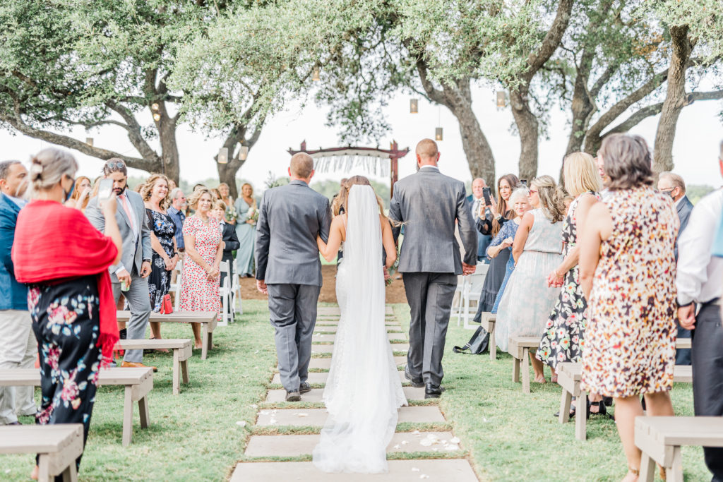 Bride and Both Fathers Walking Down Aisle Ceremony Lace Dress Cathedral Veil | Stonehouse Villa in Driftwood TX by DFW Dallas Fort Worth wedding photographer Karina Danielle Photography