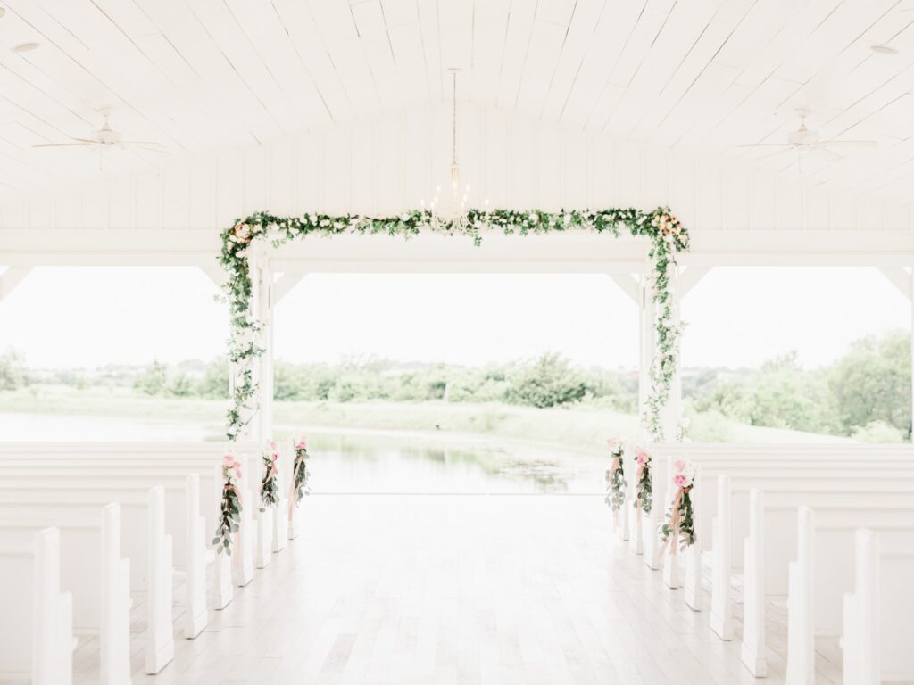 Greenery and floral installation in open air chapel at the Grand Ivory in Dallas, with white church pews for guests to sit at the venue.