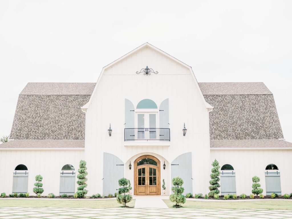Exterior of the French Farmhouse Dallas wedding venue, a white barn with grey roof and lattice grass.