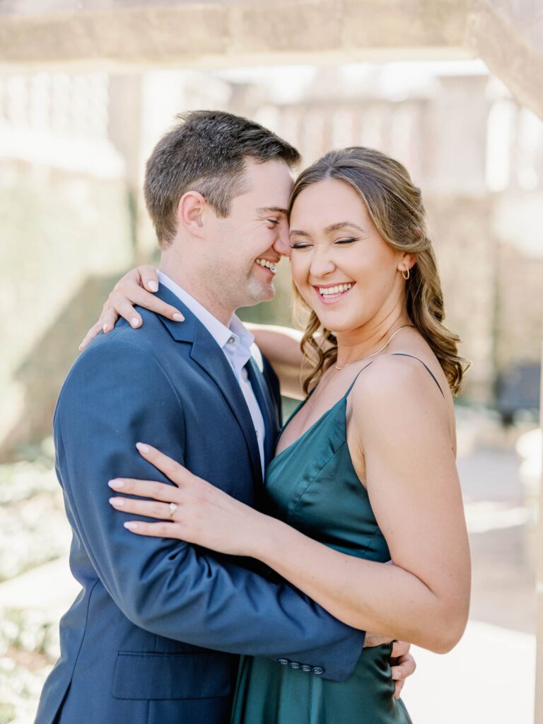 Couple in formal attire embracing and laughing taking their engagement photos at the Dallas Arboretum.