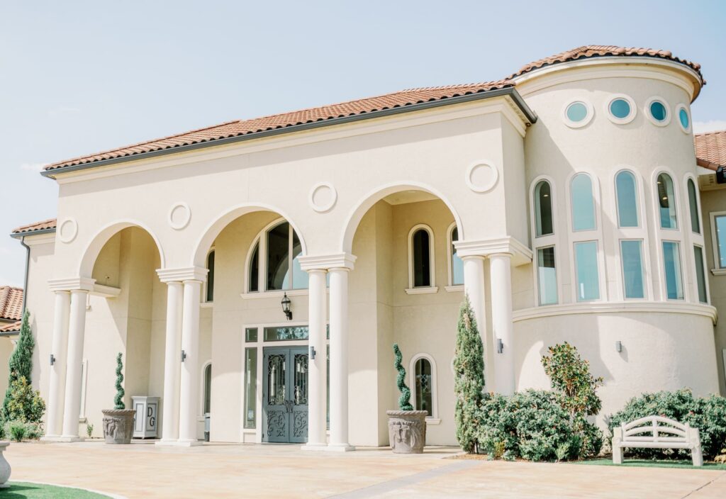 Exterior of wedding venue D'vine Grace Vineyard with stucco roof and white columns.