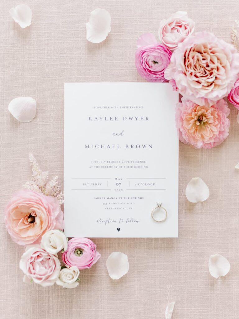 Classic white wedding invitation with surrounded by blush florals and petals.