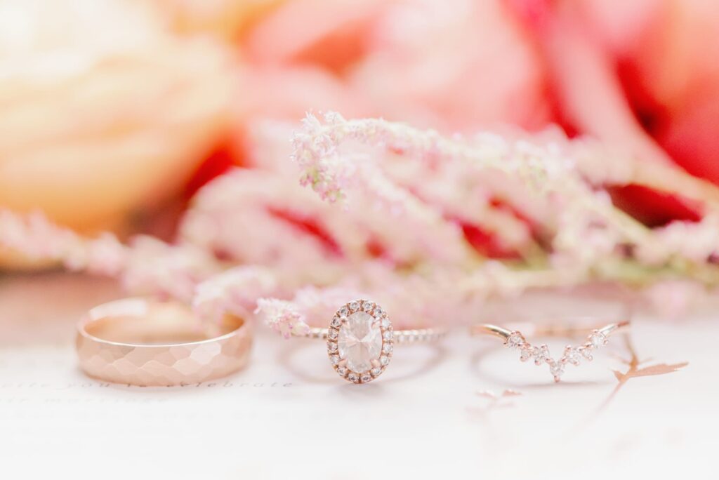 Set of rose gold wedding ring, engagement band and sunset colored florals.